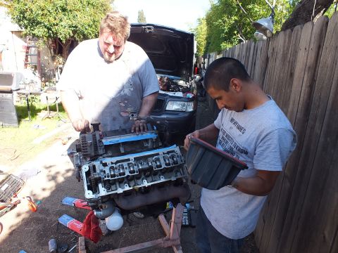 2003 Ford Crown Victoria - Helper holds a storage bin of parts as a man works the cylinder head of a disassembled V8