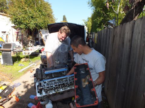 2003 Ford Crown Victoria - red valve cover is held up beside the open V8 block during a backyard engine rebuild