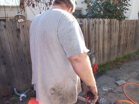 2003 Ford Crown Victoria - Back view of a man leaning over tools and parts beside a wooden fence during outdoor mechanical work