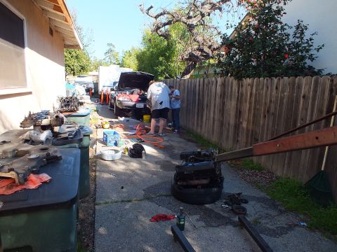 2003 Ford Crown Victoria - Wide view of a cluttered repair scene: parts on bins, hoses on the ground and a vehicle being worked on ahead