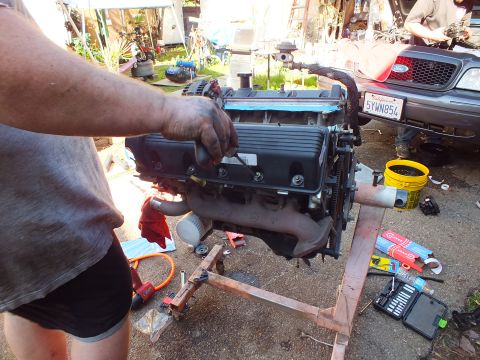 2003 Ford Crown Victoria - Disassembled V8 on a timber stand with tools laid out; a gray Ford with plate 5YWN854 sits in the background
