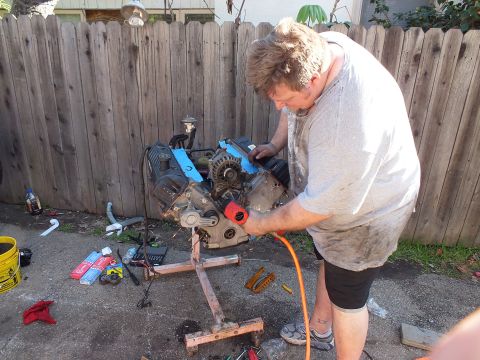 2003 Ford Crown Victoria - Worker leans in with an air tool to free a component from the V8 block on its timber stand
