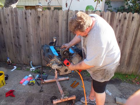2003 Ford Crown Victoria - Mid-teardown: a worker drives a red air tool into the V8 as parts lie scattered on the concrete