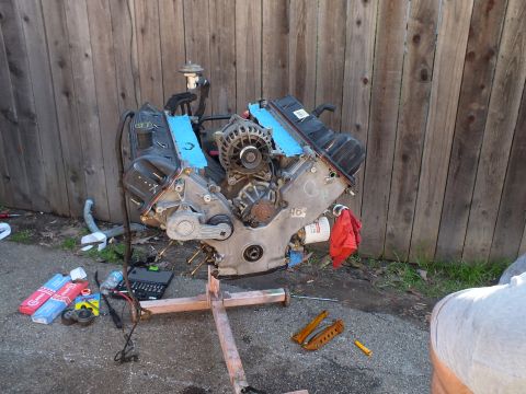 2003 Ford Crown Victoria - Unattended V8 on its timber stand, valve covers off and tools and part boxes spread across the pavement