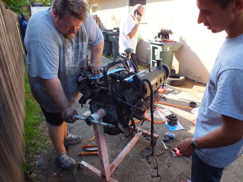 2003 Ford Crown Victoria - worker and helper rotate the V8 on its homemade stand with a steel bar as a third person stands behind