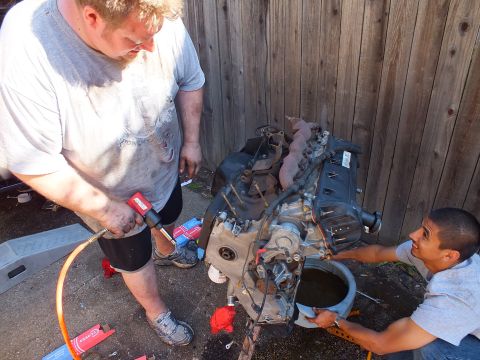 2003 Ford Crown Victoria - Two workers free parts from the bare V8 on its stand while a pan catches fluid below