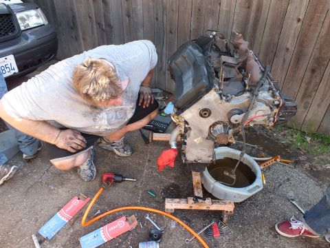 2003 Ford Crown Victoria - Engine on stands beside a drain pan during teardown, hand tools scattered across concrete