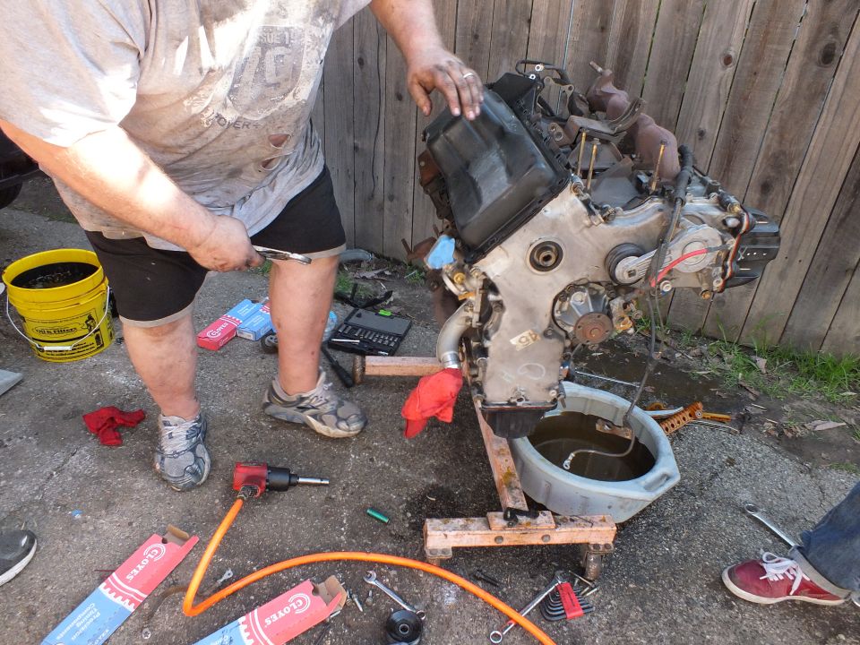 Person lifting a black engine cover off a partially stripped engine in a backyard