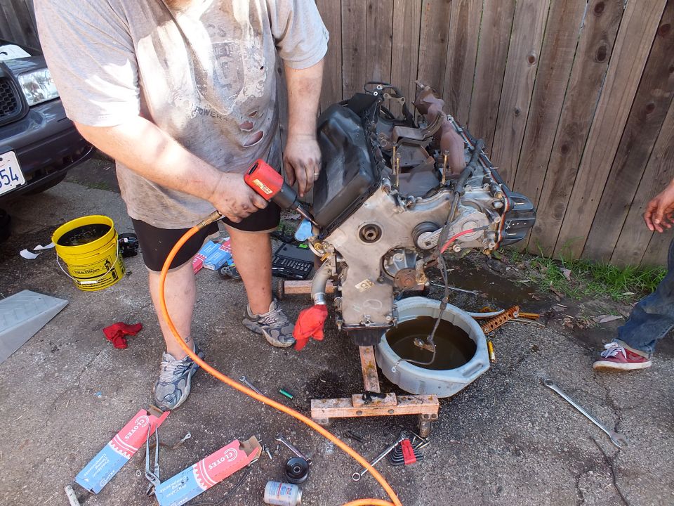 Man using a red impact wrench on a removed engine over an oil drain pan