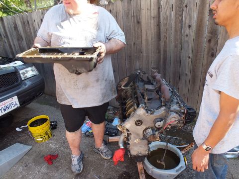 2003 Ford Crown Victoria - Oil pan held up showing residue, removed from the engine block visible in the background