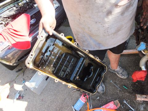 2003 Ford Crown Victoria - Oil pan interior with baffle shown, parked vehicle and Ford emblem behind the worker