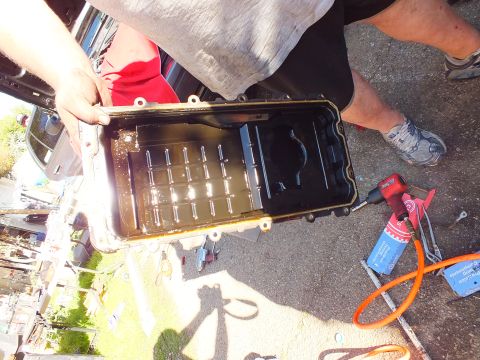 2003 Ford Crown Victoria - Oil pan held upright revealing the internal baffle, tools and air hose on the ground below