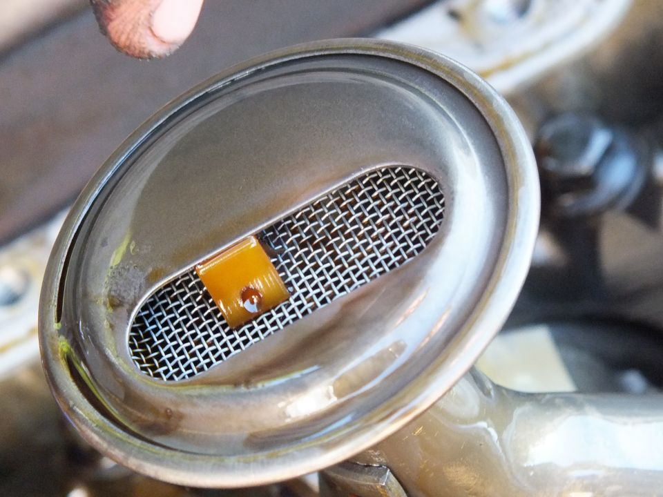 Close-up of an oil pickup screen with orange debris caught in the mesh