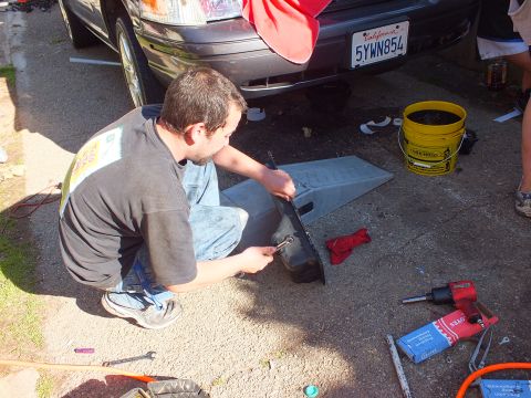 2003 Ford Crown Victoria - Worker servicing a vehicle's rear bumper area, California plate 5YWN854 above, ramp at right