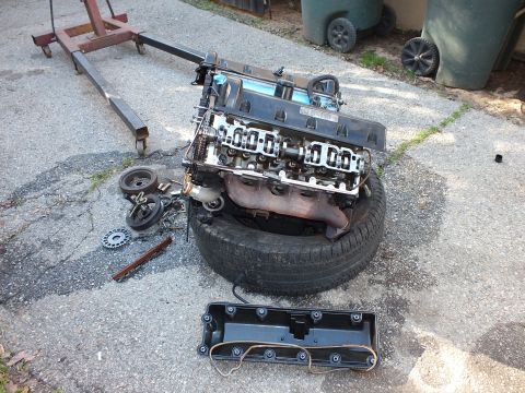 2003 Ford Crown Victoria - Cylinder head with rocker arms exposed sitting on a tire, valve cover and timing parts nearby