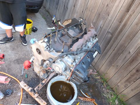 2003 Ford Crown Victoria - Complete engine assembly staged on wood blocks over a drain pan during a backyard rebuild