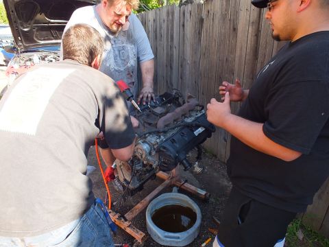 2003 Ford Crown Victoria - Group of three working a removed engine with an impact wrench above an oil drain pan