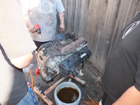 2003 Ford Crown Victoria - Removed engine worked with a red impact wrench, oil drain pan beneath, fence behind