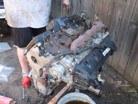2003 Ford Crown Victoria - Side profile of a removed engine showing intake and rusty exhaust manifolds during teardown