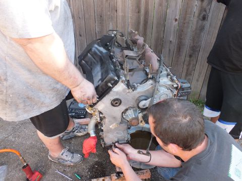 2003 Ford Crown Victoria - Crew stripping components from an engine block staged over a drain pan in a backyard