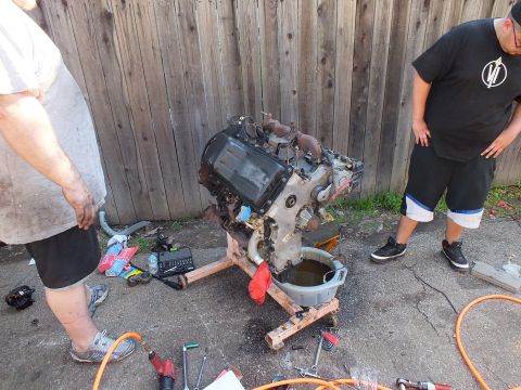 2003 Ford Crown Victoria - Bare engine resting on improvised cradle, drain pan of used oil below, scattered hand tools