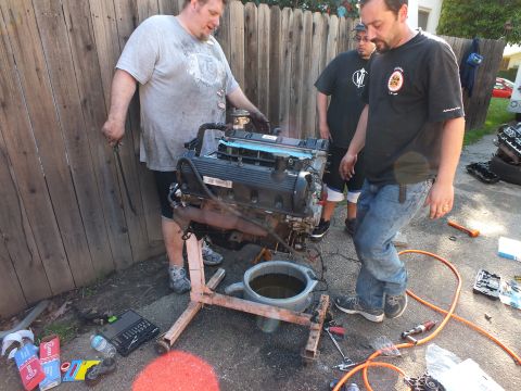 2003 Ford Crown Victoria - Long-block engine on a homemade stand by a fence as three men inspect it in a driveway
