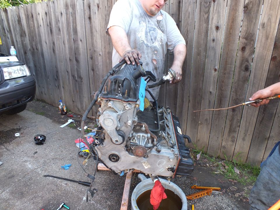 Man in dirty shirt working on inverted engine block on cradle beside wooden fence