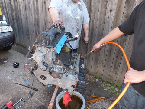 2003 Ford Crown Victoria - Bare engine on a homemade stand being blown out with an air line over a used-oil bucket