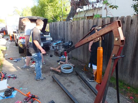 2003 Ford Crown Victoria - Group setting up a red shop crane with orange hydraulic ram beside a hood-up vehicle