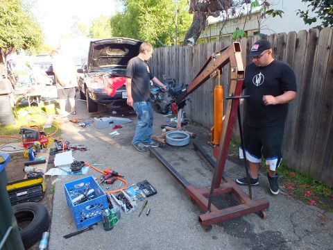 2003 Ford Crown Victoria - Red folding engine hoist staged in a driveway with milk crate of tools and tires nearby