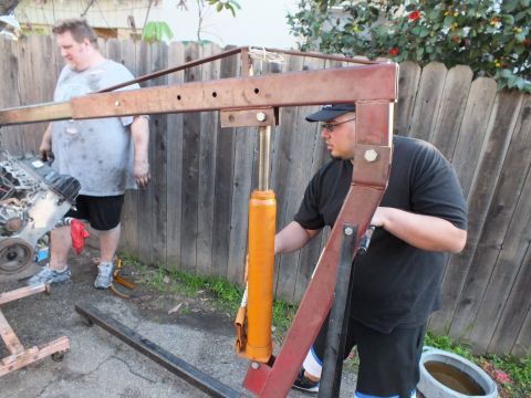 2003 Ford Crown Victoria - Man working the orange hydraulic cylinder of a red engine crane against a wooden fence