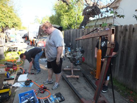 2003 Ford Crown Victoria - Engine on a stand with a red shop crane and tool kits laid out across a backyard driveway