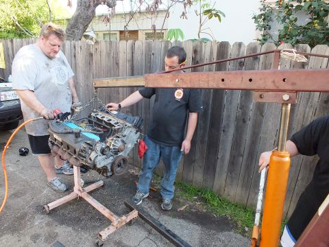 2003 Ford Crown Victoria - Engine on a homemade stand under the boom of a red shop crane as two men look it over