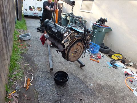 2003 Ford Crown Victoria - Engine hangs from a lifting chain in a driveway while a worker stands behind it; oil drain pan below.