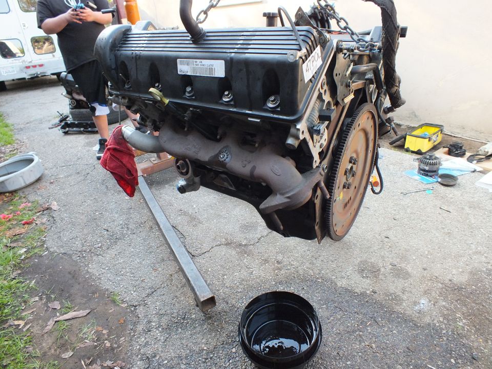 V6 engine on hoist showing valve cover exhaust manifold and flywheel close up