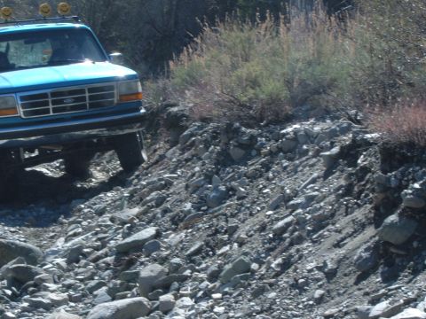1988 Ford Bronco - A blue Ford Bronco navigates a rocky trail, its off-road capabilities evident.