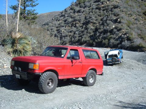1988 Ford Bronco - Two SUVs are parked on a gravel road in a dry, mountainous area.
