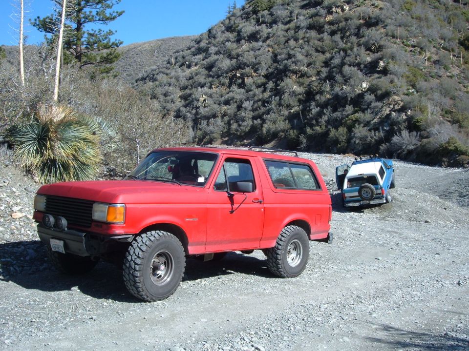 Red Ford Bronco parked on a dirt road with another blue SUV behind it