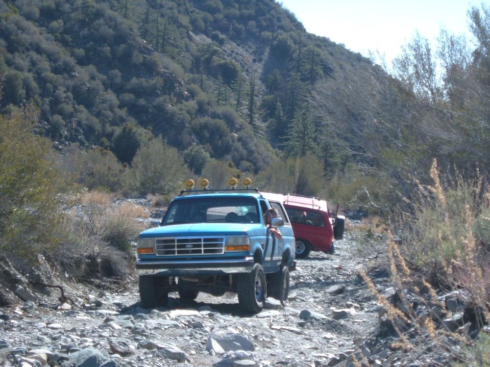 Blue SUV with off-road lights on roof rack driving on rocky terrain