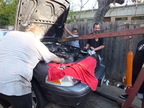 2003 Ford Crown Victoria - Several men guide an engine down into the bay of a gray SUV with a red cloth protecting the front fender.