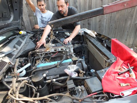 2003 Ford Crown Victoria - Two men lean over a crowded engine bay routing parts; a red shop cloth covers the fender beside the radiator.