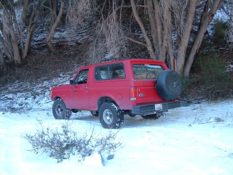 1988 Ford Bronco - A red Ford Bronco sits in a snowy, wooded area with bare trees.