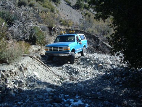 1988 Ford Bronco - A blue Ford Bronco navigates a challenging, rocky terrain in a mountainous area.