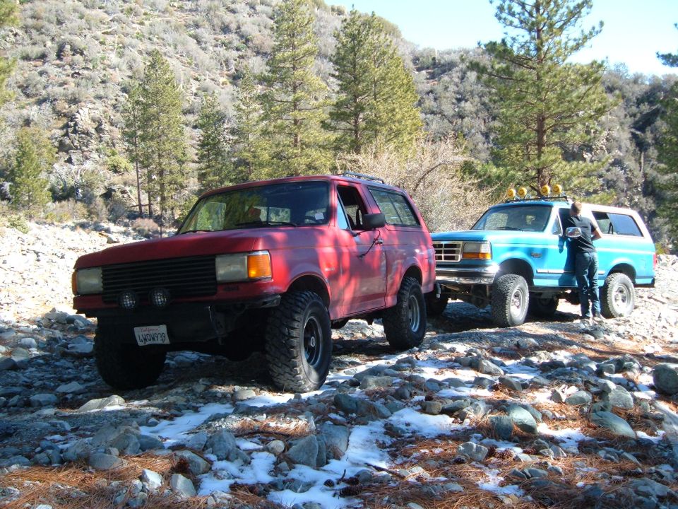 Red 1987-1991 Ford Bronco parked on a rocky trail next to a blue Bronco