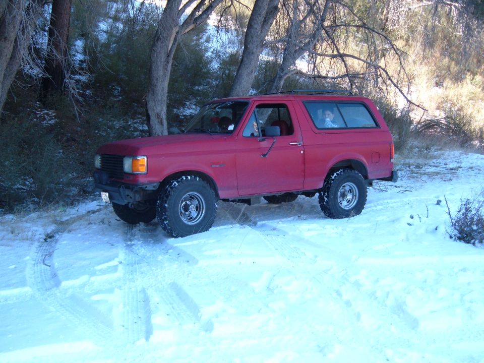 Red SUV with aftermarket wheels and tires in snow, front grille visible