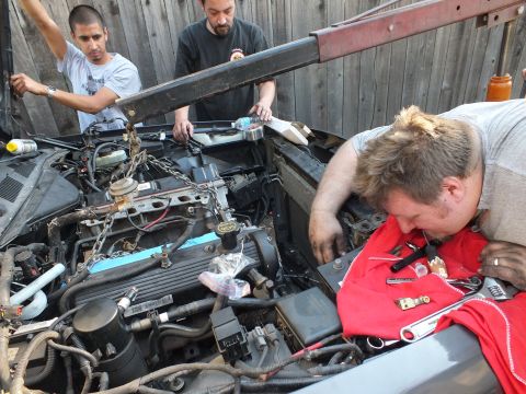 2003 Ford Crown Victoria - Workers position lifting chains over an engine while another reaches into the bay near the valve cover.