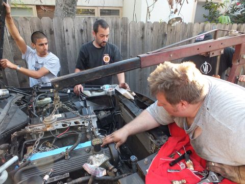 2003 Ford Crown Victoria - Workers seat an engine into the bay as a hoist beam and a red ladder rest against the wood fence.