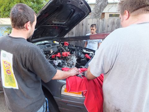 2003 Ford Crown Victoria - Three men work at the open hood of a gray SUV, draping a red cloth across the front during engine work.