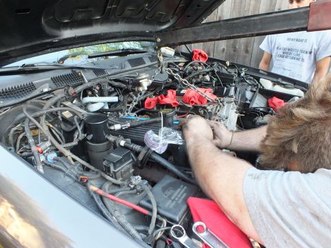2003 Ford Crown Victoria - Hands route connections over a Ford engine; red shop cloths and box-end wrenches lie across the fender.