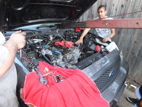2003 Ford Crown Victoria - young man stands at the open engine bay of a gray Ford SUV, red cloth over the grille and tools laid out.
